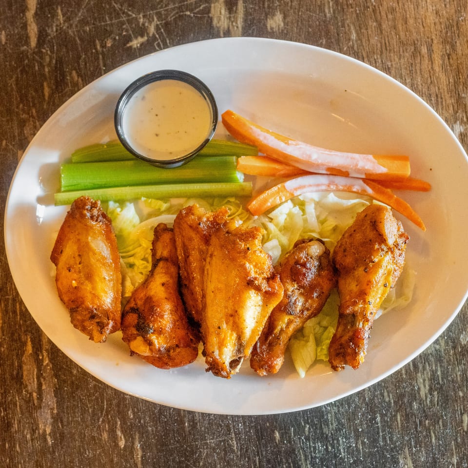 Plate of grilled chicken wings with celery, carrot sticks, lettuce, and dipping sauce on a wooden table.